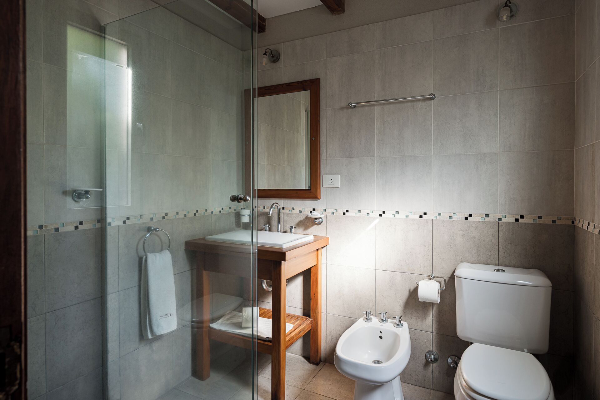 A bathroom with a glass shower enclosure, a wooden vanity with a sink, a bidet, and a toilet.