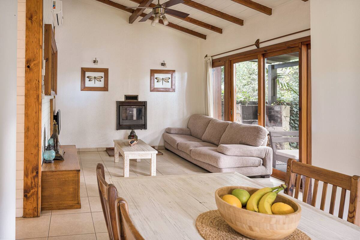 A living room with a sofa, a television, a dining table with chairs, and a window with a view of greenery.