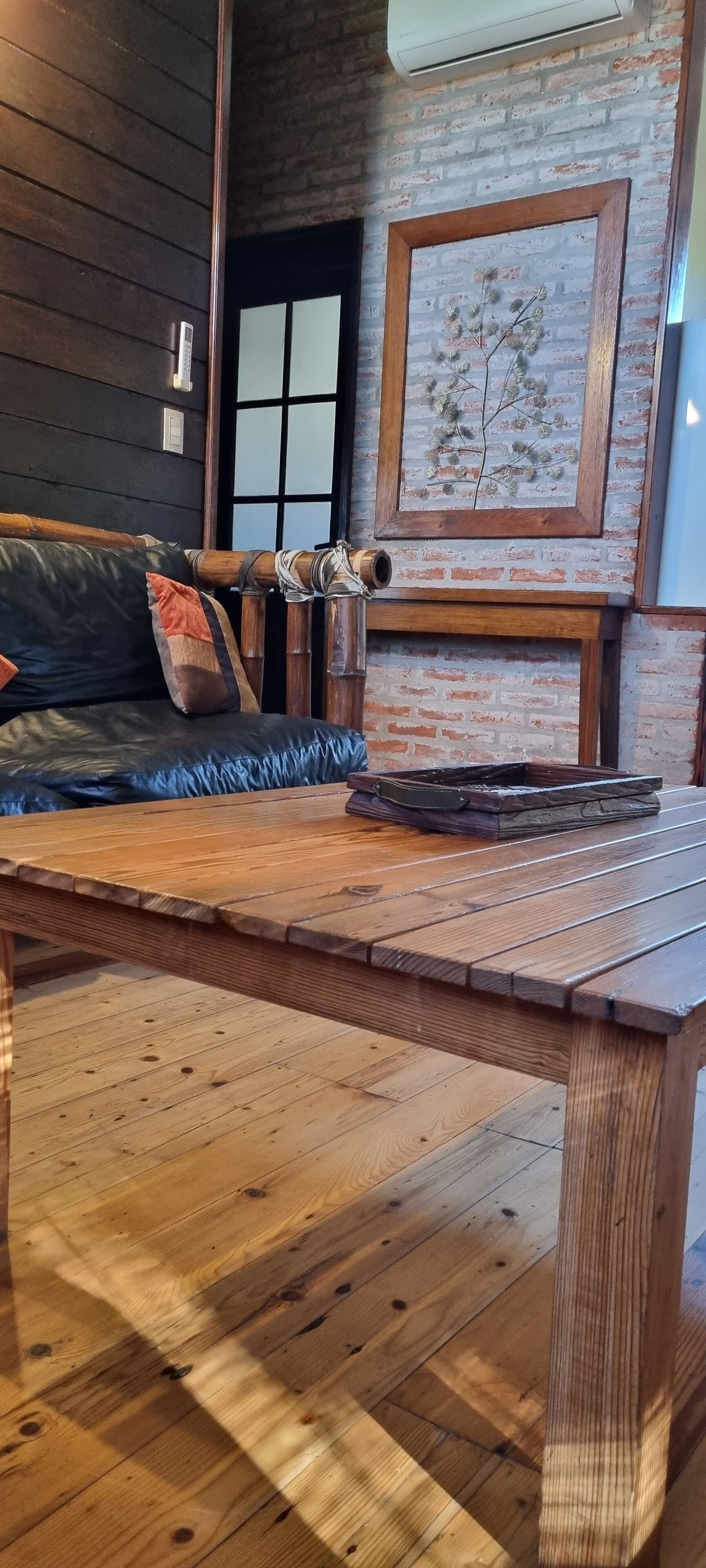 Una mesa de madera en una habitación con pared de ladrillo y un cuadro enmarcado.