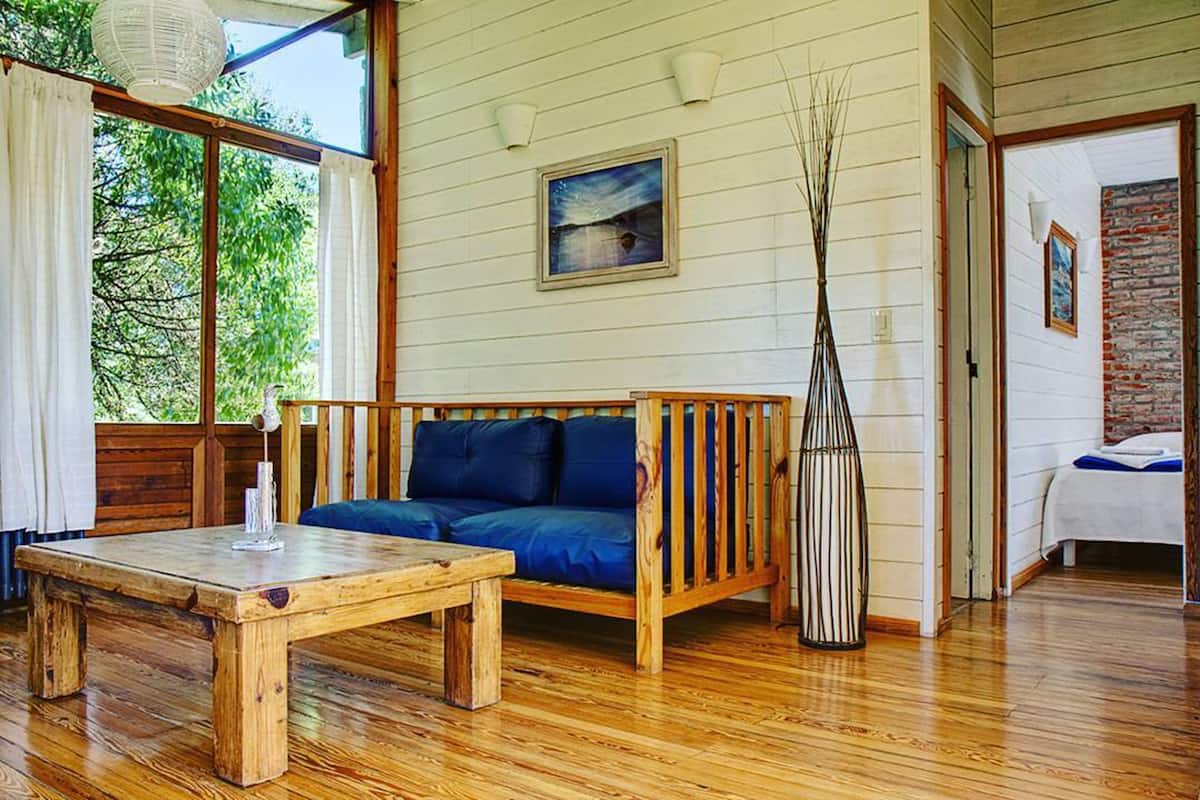 A room with a wooden floor, a wooden sofa with blue cushions, a wooden coffee table, and a tall vase.