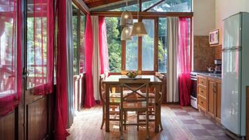 A kitchen with wooden cabinets, a dining table with chairs, a refrigerator, and a window with curtains.