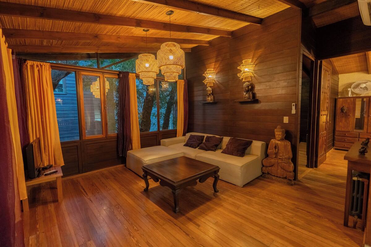 A cozy living room with a wooden floor, a beige sectional sofa, a coffee table, and a Buddha statue.