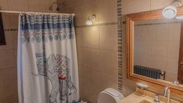 Un baño con cortina de ducha de diseño de elefante, inodoro, lavabo con espejo y suelo de baldosas.