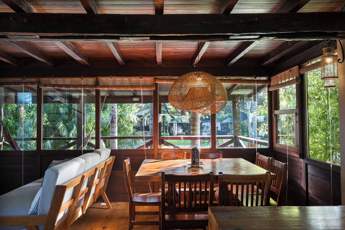 A wooden interior with a dining table, chairs, a bench, and a large woven lamp.