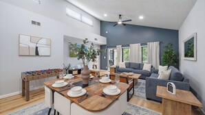 A modern living room with a foosball table, a dining area with a wooden table and chairs, and a gray sofa.