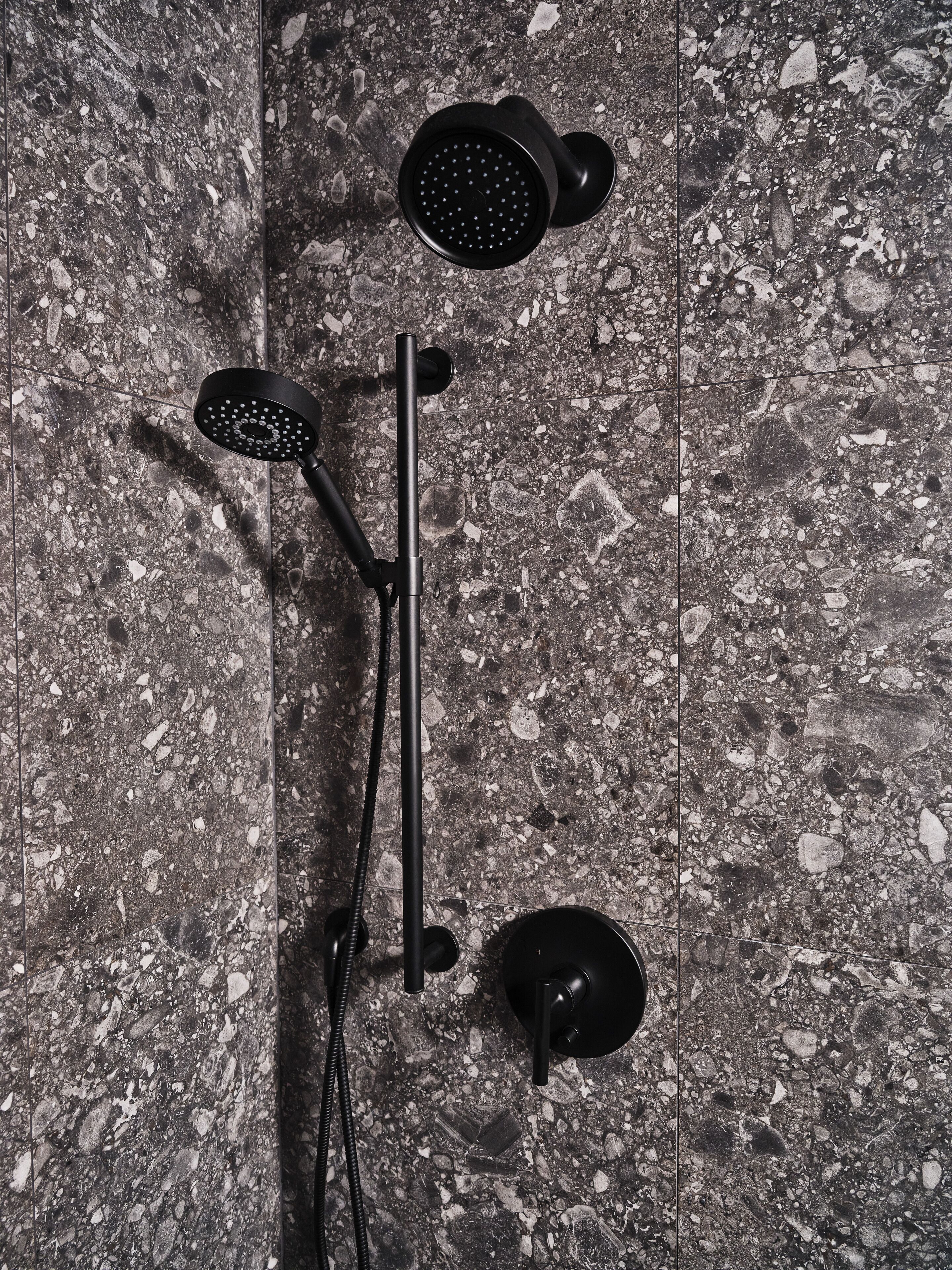 A shower with a handheld and a stationary head, mounted on a wall with a speckled tile pattern.