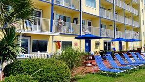 Un hotel de varios pisos con balcones, mobiliario exterior y un jardín bien cuidado.
