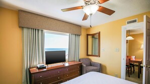 Habitación de hotel con cama, cómoda, televisor, ventilador de techo y vista al océano.