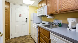 A compact kitchen with wooden cabinets, a white refrigerator, a stove, a sink, and a coffee maker.
