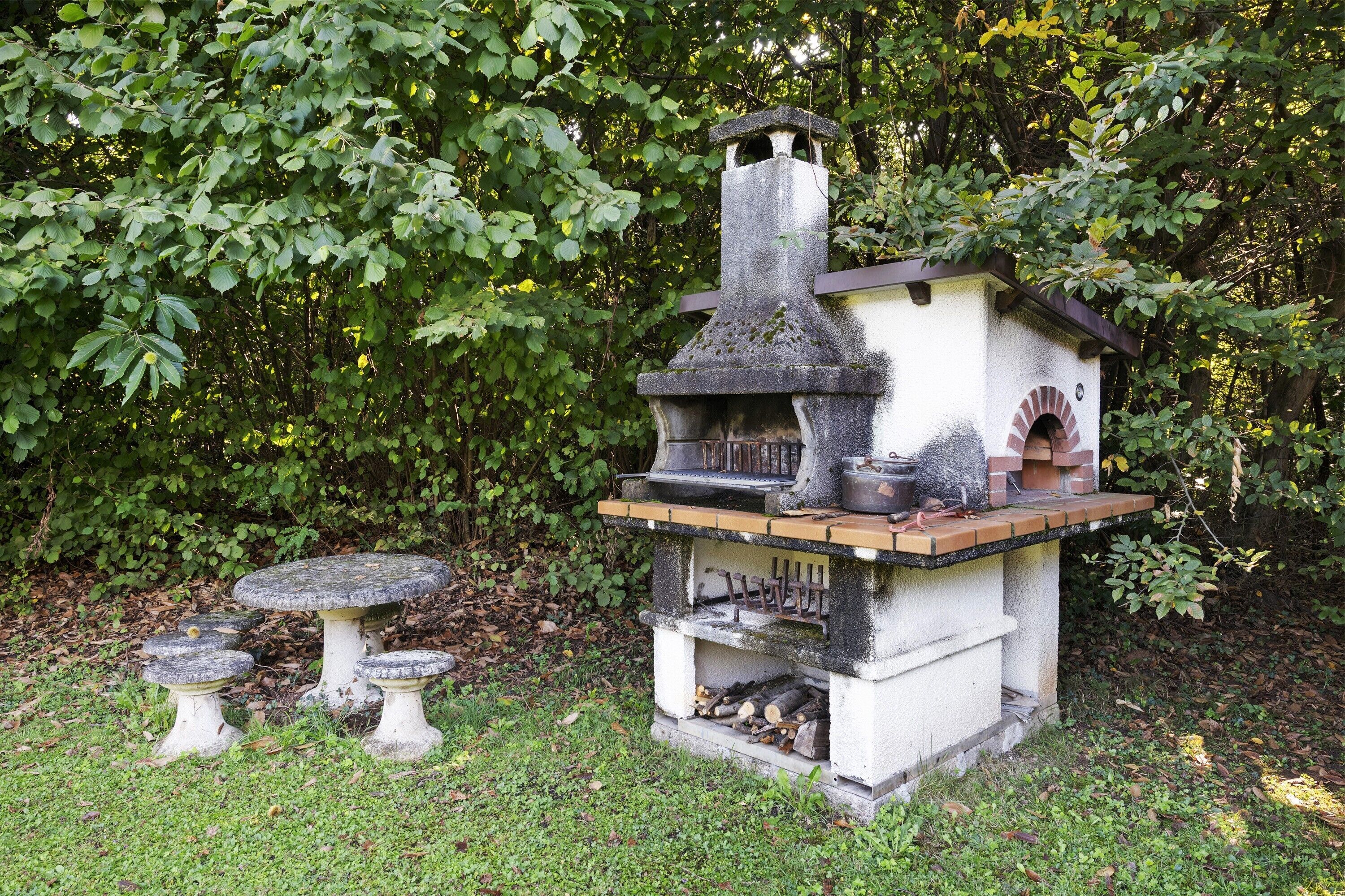 A stone outdoor kitchen with a chimney, a table, and two stools.