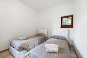 Une chambre avec deux lits, une fenêtre et un mur blanc.