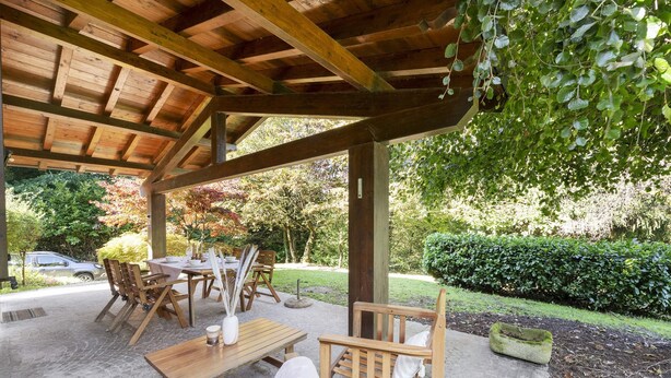 A covered outdoor seating area with wooden furniture, a table, and chairs.