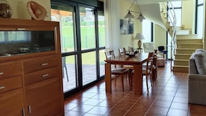 A spacious living area with a dining table, sofa, and a staircase leading to an upper level.