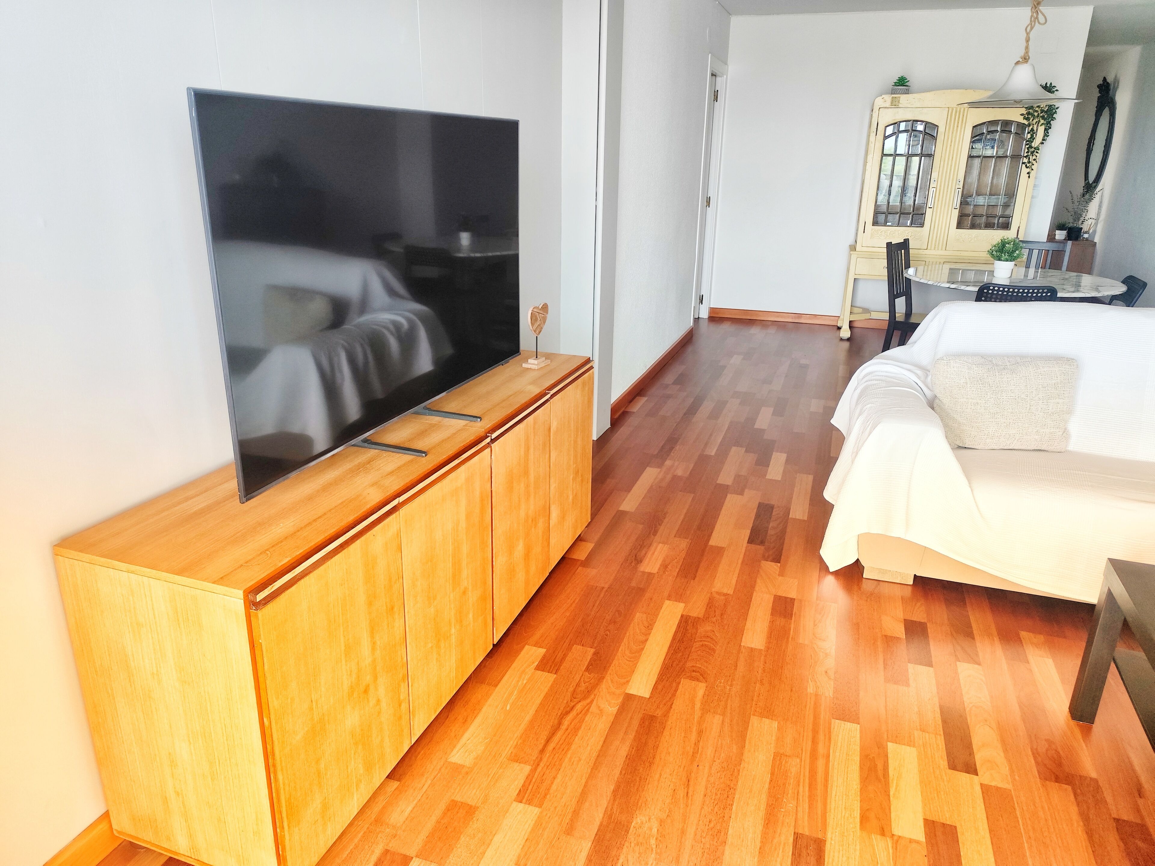 Habitación de hotel moderna con un televisor de pantalla plana grande montado en un mueble de madera, una cama con ropa de cama blanca y suelo de madera.