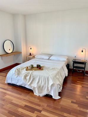 A bedroom with a bed, bedside tables, a mirror, and a shelf.