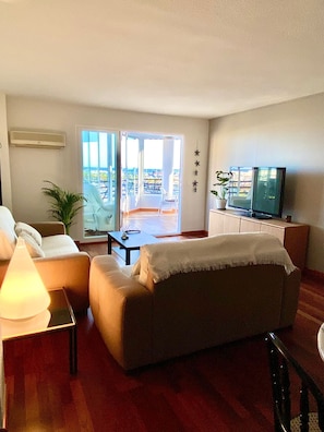 A living room with a sofa, a TV, a lamp, and a view of the outside.