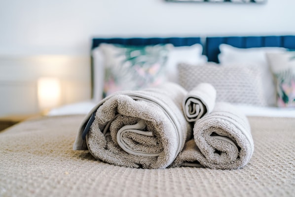 A neatly made bed with rolled towels and a blue headboard.