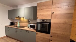 A modern kitchen with grey cabinets, a wooden accent wall, a built-in oven, and a microwave.