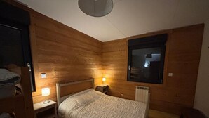 A cozy wooden room with a bed, a nightstand, a window, and a radiator.