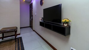 Un couloir avec un téléviseur fixé au mur, un banc et un vase de fleurs.