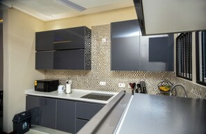 Une cuisine moderne avec des meubles de couleur sombre, un four à micro-ondes, une bouilloire et un dosseret carrelé.