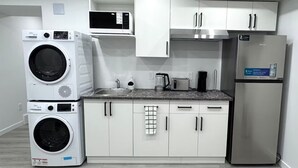 A compact kitchen with a washing machine, microwave, toaster, and refrigerator. - Amazing 2-Bedroom Basement Suite (Winnipeg)