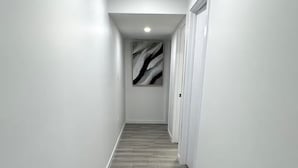 A hallway with a wooden floor, white walls, and a ceiling light. - Amazing 2-Bedroom Basement Suite (Winnipeg)