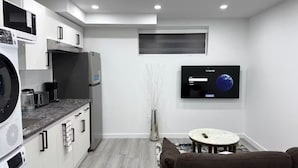 A compact kitchen with modern appliances, a dining area with a round table, and a flat-screen TV mounted on the wall. - Amazing 2-Bedroom Basement Suite (Winnipeg)