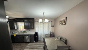 A modern kitchen with dark cabinets, a dishwasher, and a dining area with a table and chairs.
