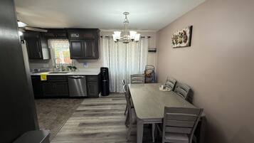 A modern kitchen with dark cabinets, a dishwasher, and a dining area with a table and chairs.