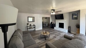 A modern living room with a fireplace, grey sofas, a coffee table, and a flat-screen TV mounted above the fireplace.