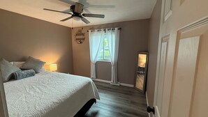 A bedroom with a bed, a ceiling fan, a window with curtains, and a nightstand with a lamp.