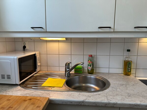 A kitchen with white cabinets, a stainless steel sink, a microwave, a yellow sponge, and two bottles of olive oil.