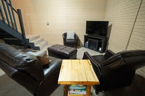 A living room with a brick wall, a staircase, a leather sofa, a wooden coffee table, and a television.