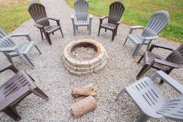 Eine runde Sitzgruppe um ein Lagerfeuer mit Stühlen und Holzscheiten.