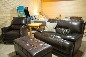 Ein Wohnzimmer mit einer Ledersofa, passendem Hocker, einem Gaming-Sessel und einem kleinen Holztisch.