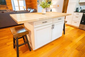 A kitchen with a wooden countertop, white cabinets, a bench, and a potted plant.