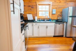 A kitchen with wooden walls, a window, a stainless steel refrigerator, and a sink.