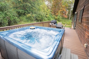 A hot tub on a wooden deck with a view of a forested area.