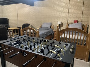 A room with a foosball table, two beds, a TV, and a brick-patterned wall.