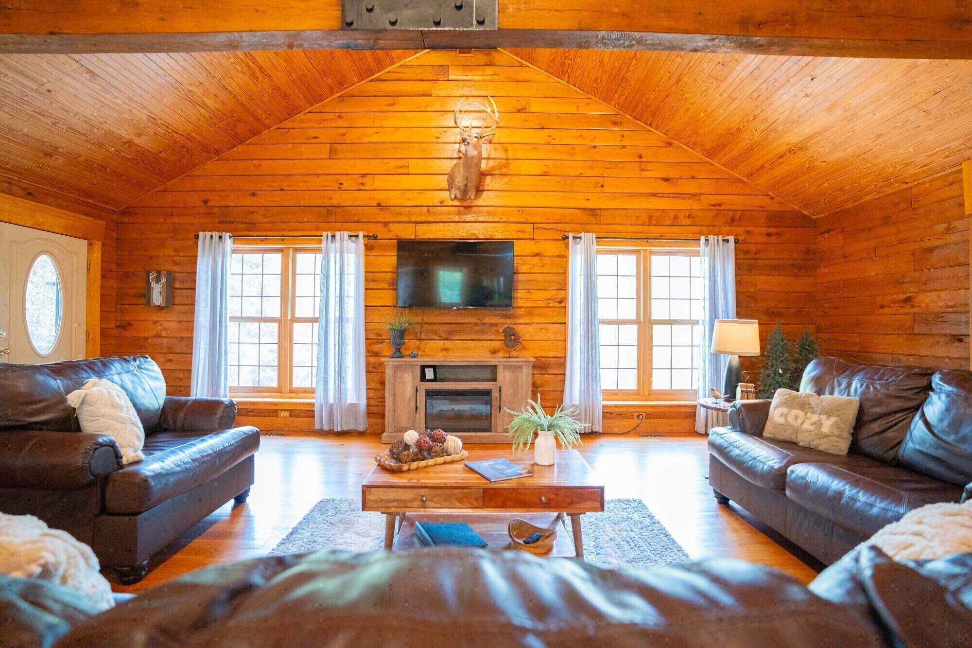 A log cabin interior with a fireplace, leather sofas, a coffee table, and a television.