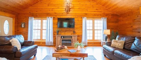 A log cabin interior with a fireplace, leather sofas, a coffee table, and a television.