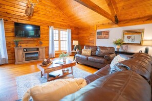 Ein Holzblockhaus-Interieur mit Kamin, Ledersofa, Holzdielen und einem Fernseher.