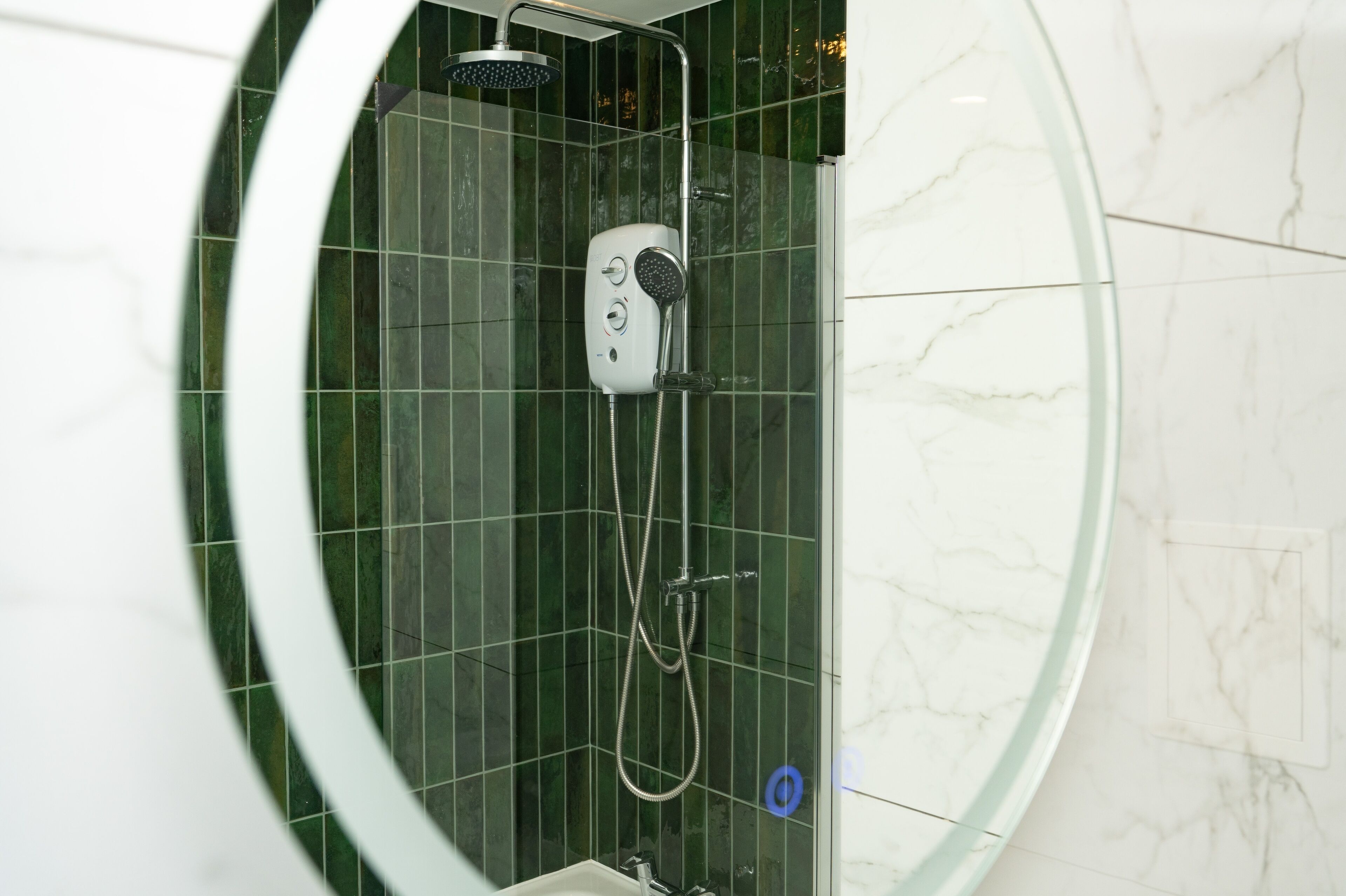 Une douche moderne dotée d’un pommeau de douche à main et d’un pommeau de douche fixe fixé au mur, le tout installé sur un mur recouvert de carreaux verts.