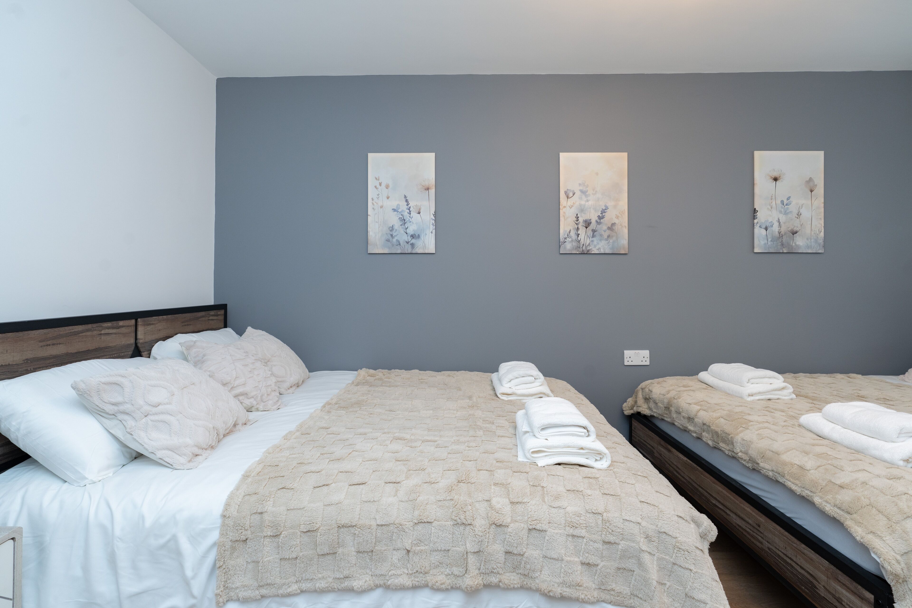 Quarto de hotel com duas camas, uma parede cinzenta e três quadros.