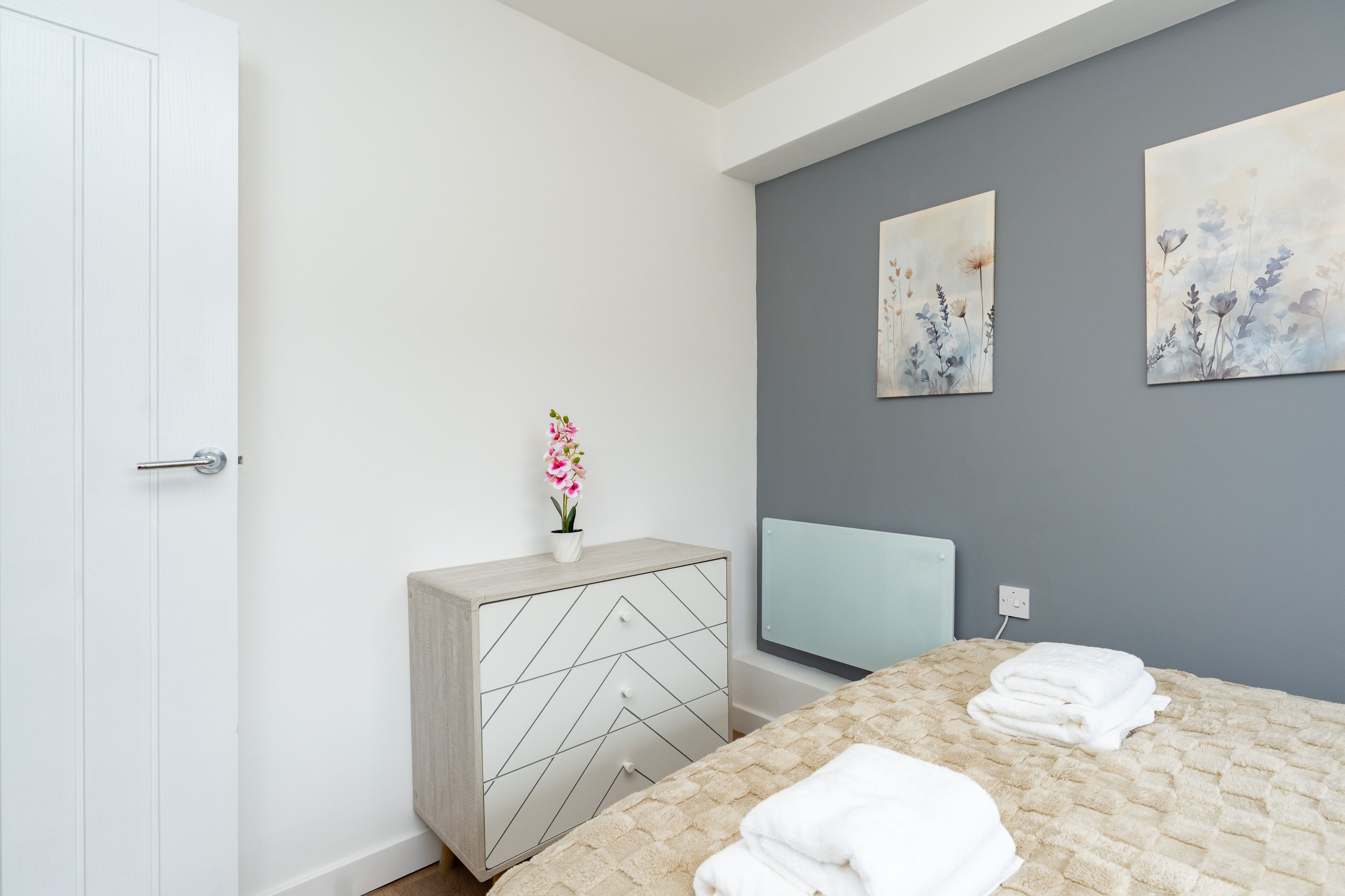 A modern bedroom with a bed, a dresser, a TV, and artwork on the wall.