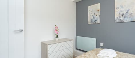 A modern bedroom with a bed, a dresser, a TV, and artwork on the wall.
