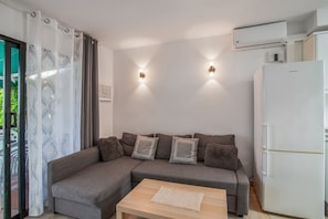 Una sala de estar moderna con un sofá seccional gris, una mesa de centro de madera y un refrigerador blanco.