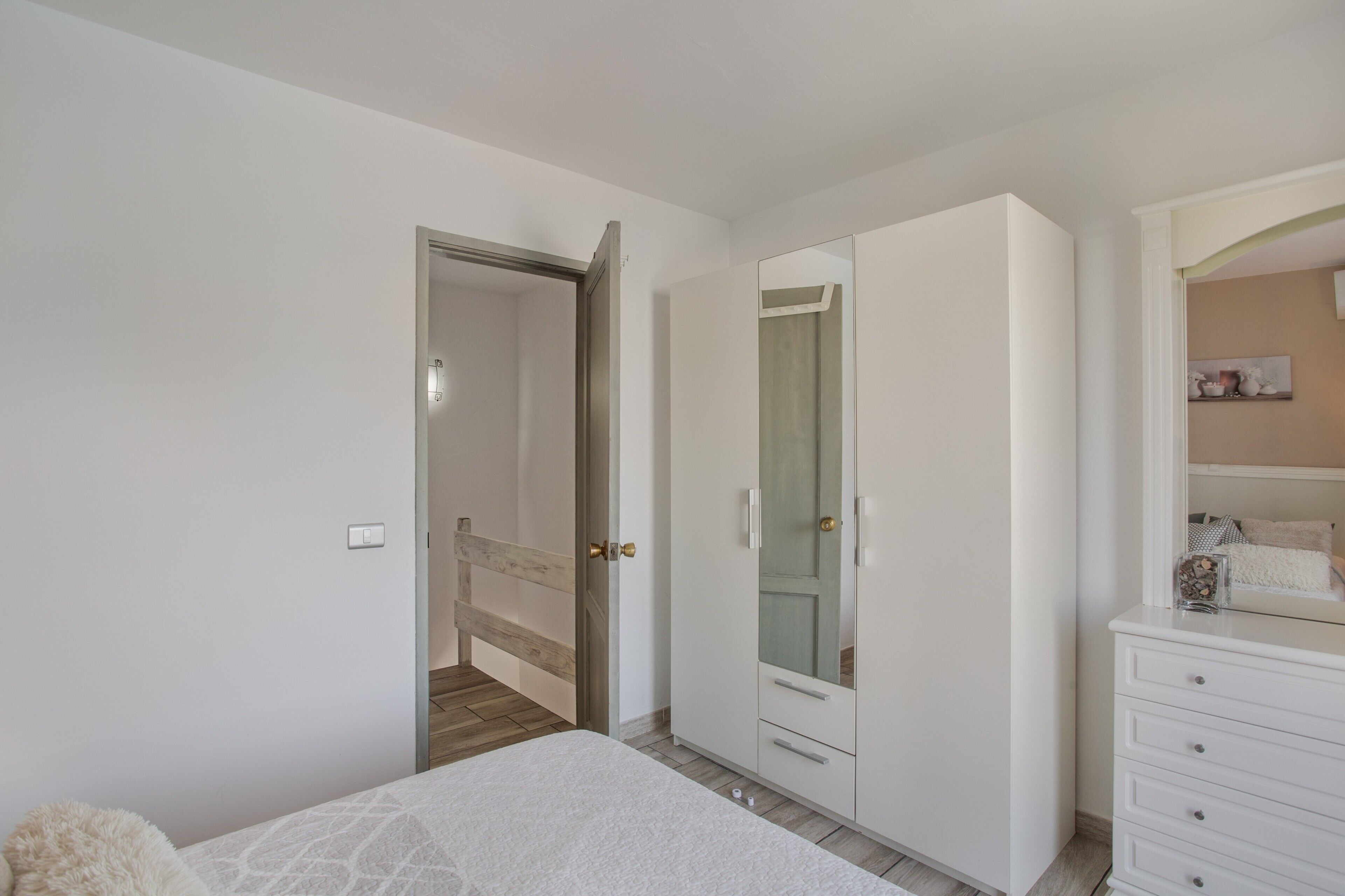 A bedroom with a bed, a wardrobe, a mirror, and a door leading to another room.