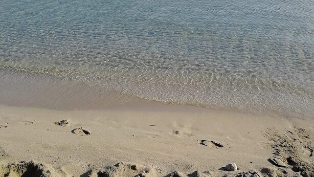 A beach with clear shallow waters and a sandy shore.